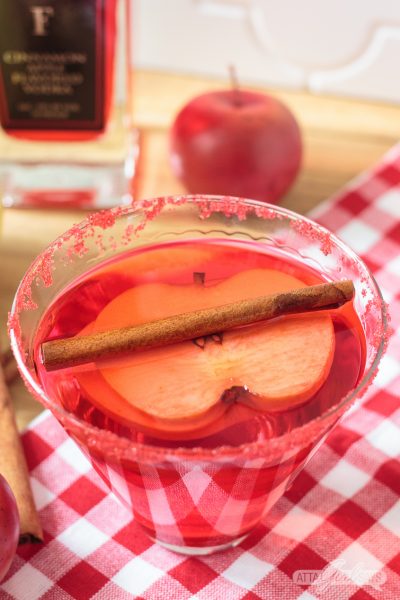 red cinnamon apple martini with an apple slice and cinnamon stick garnish