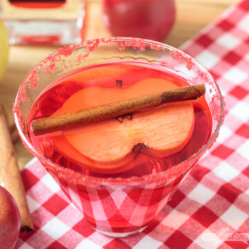 red cinnamon apple martini with an apple slice and cinnamon stick garnish