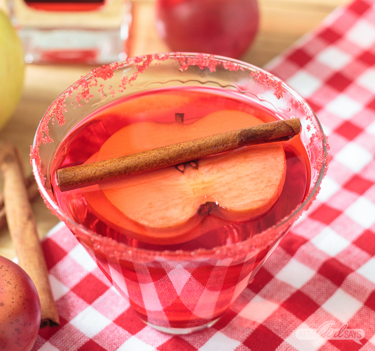 red cinnamon apple martini with an apple slice and cinnamon stick garnish