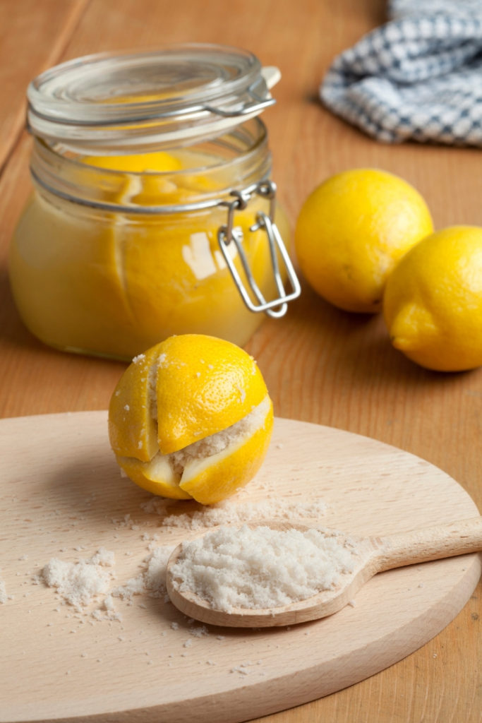 preserved lemon on a cutting board with a wooden spoon filled with salt with a jar of lemons in the background