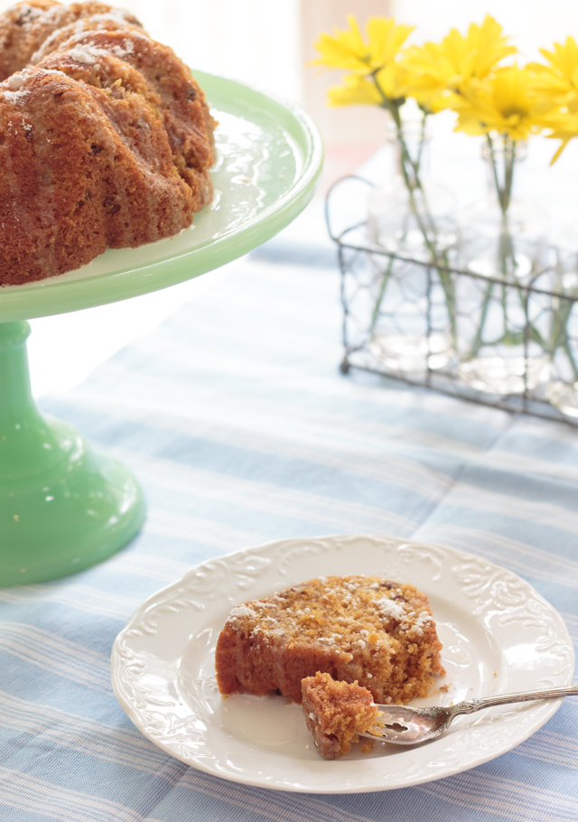 slice of carrot cake beside a cake stand with a bundt cake