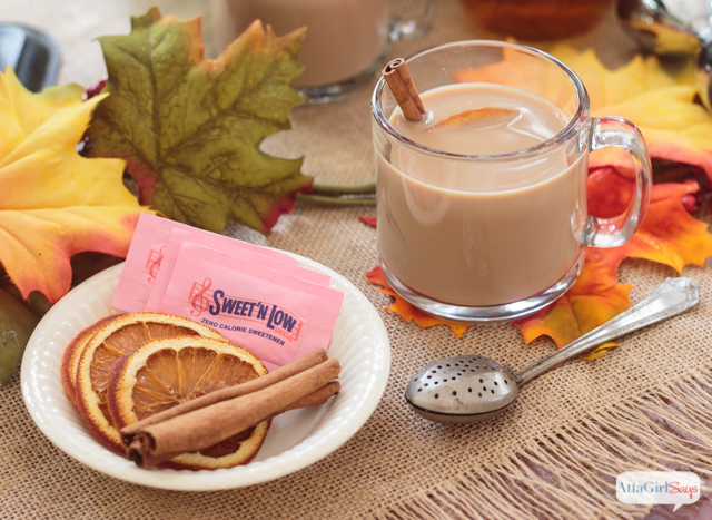 ironstone bowl with orange slices, cinnamon sticks and sweetener packets beside a mug of spiked chai tea latte