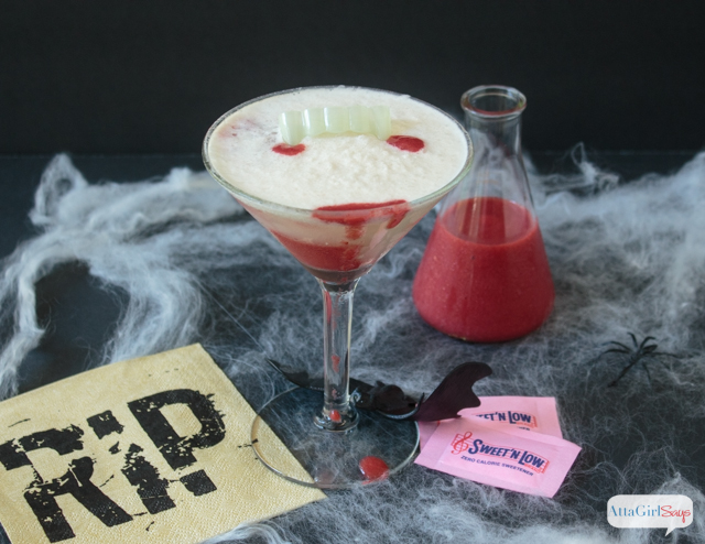 These Vampire's Kiss Halloween cocktails only look sinister! But they taste delicious. Blood-red strawberry puree pierces a creamy white homemade pina colada, in this spooky take on the popular Hawaiian Lava Flow cocktail. The right garnishes and props, like vampire teeth, plastic bats, spiderwebs and a beaker filled with strawberry puree turn it into a spooky Halloween mixed drink. #ad #donthesitaste