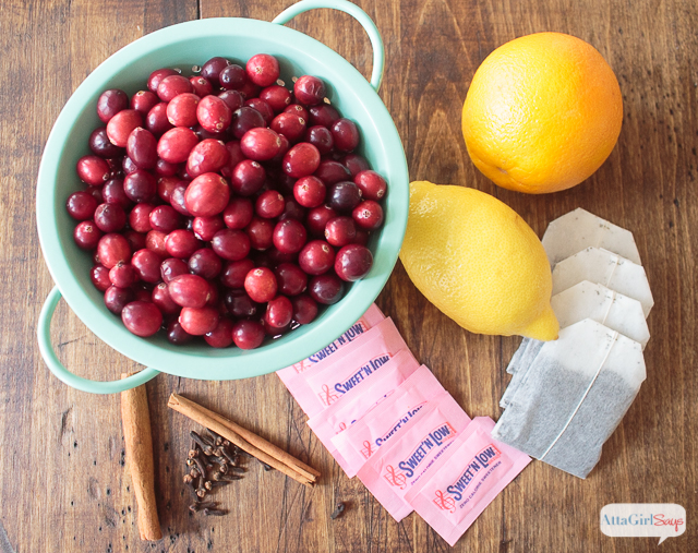 fresh cranberries in a colander with cinnamon sticks, lemons, tea bags and sweetener