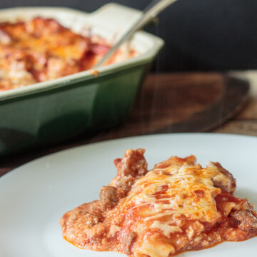 plate of cheesy homemade lasagna beside a casserole dish