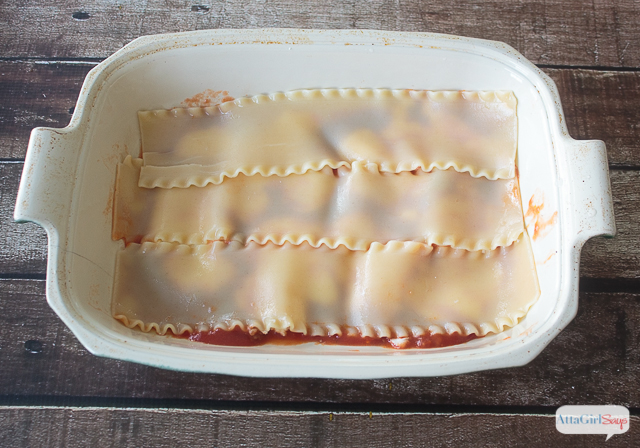 lasagna noodles layered over cheese and sauce in a casserole dish