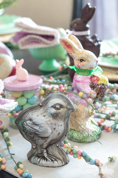 Let this pretty holiday tablescape, featuring pops of pastel and candy, inspire your own Easter table decor. I used chocolate molds, pastel candies, vintage Easter eggs, chocolate bunny figurines to create this sweet seasonal scene. #eastercandy #tablescape #eastertable #springtablescape #tabledecor