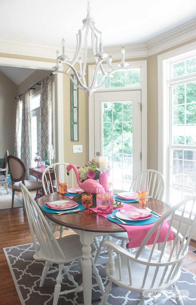 A kitchen table set for dinner, decorated with pink flamingo party supplies and pink and aqua blue linens.