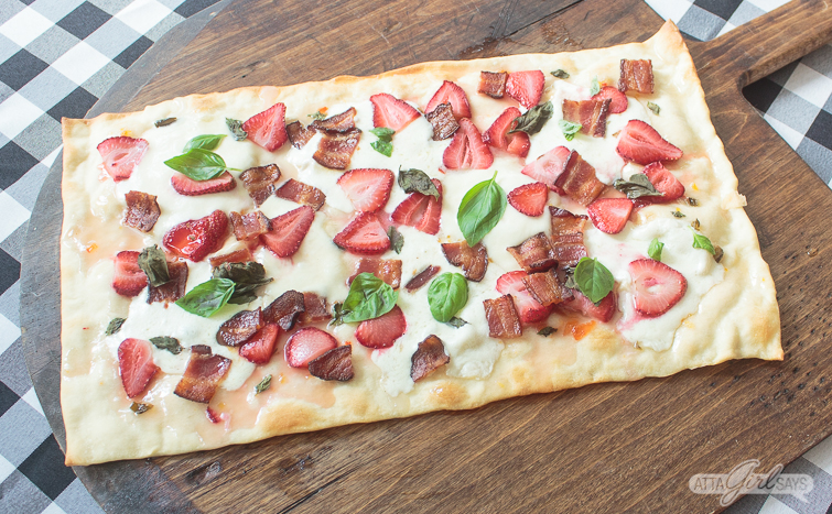 Strawberry bacon flatbread pizza with basil on a wooden pizza peel on top of a black and white gingham tablecloth