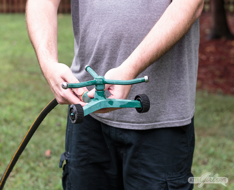 man in black shorts and a gray t-shirt attaching a sprinkler to a water house