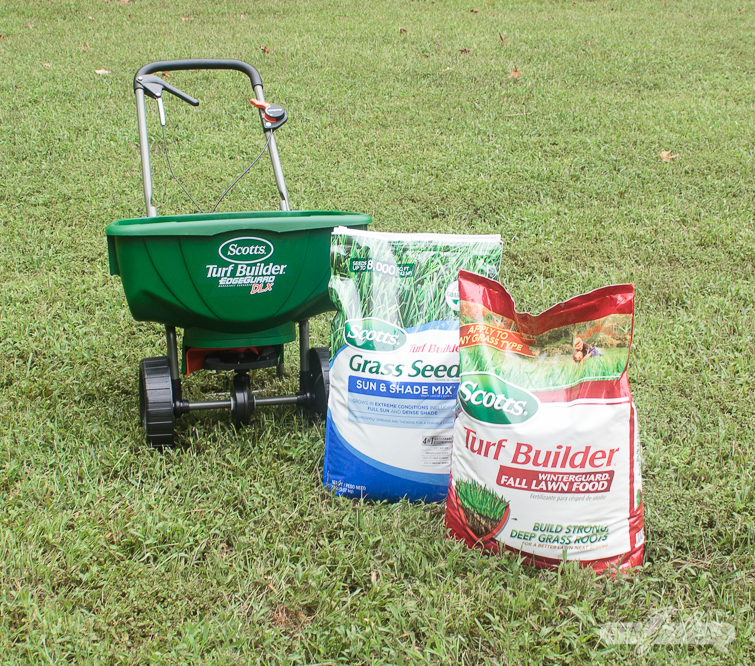 bags of grass seed and fertilizer on a lawn beside a Scotts broadcast seed spreader