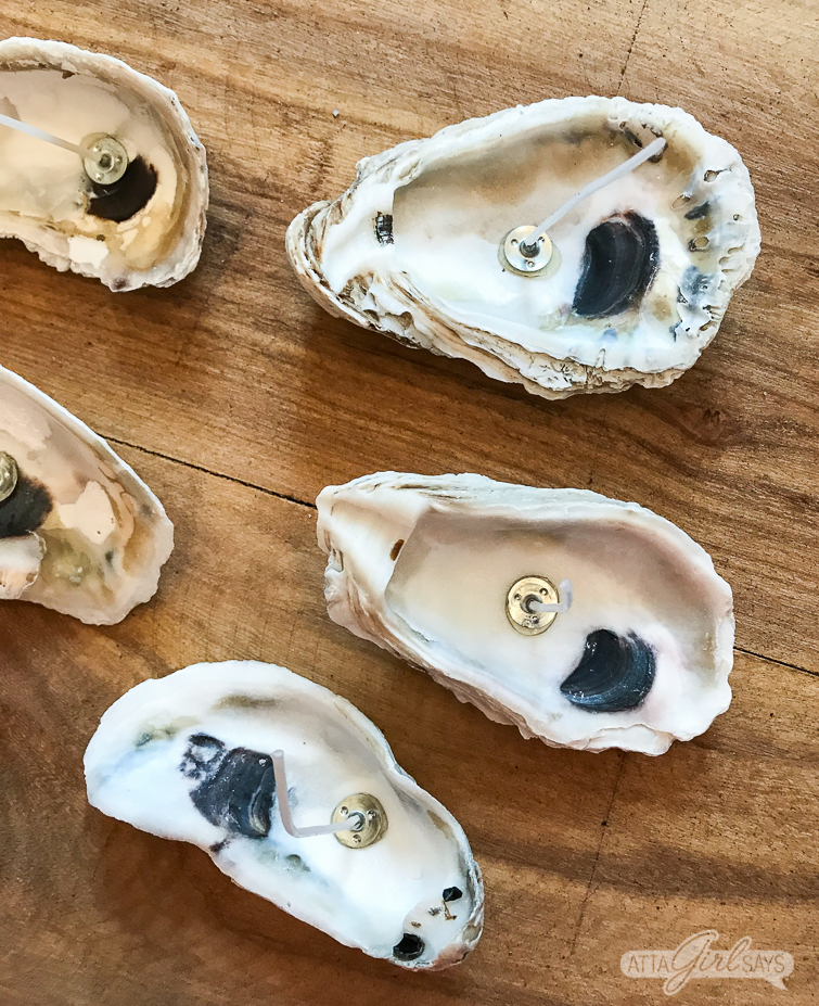 Add your favorite beach fragrance to these DIY oyster shell candles. How pretty would these be on the tables at a beach wedding or a romantic seaside dinner? #beachcrafts #seashellcrafts #oystershells #seashells #seashell #beachwedding #coastal #destinationwedding #diywedding #weddingdecor oyster shells with candle wicks in them on a wood surface
