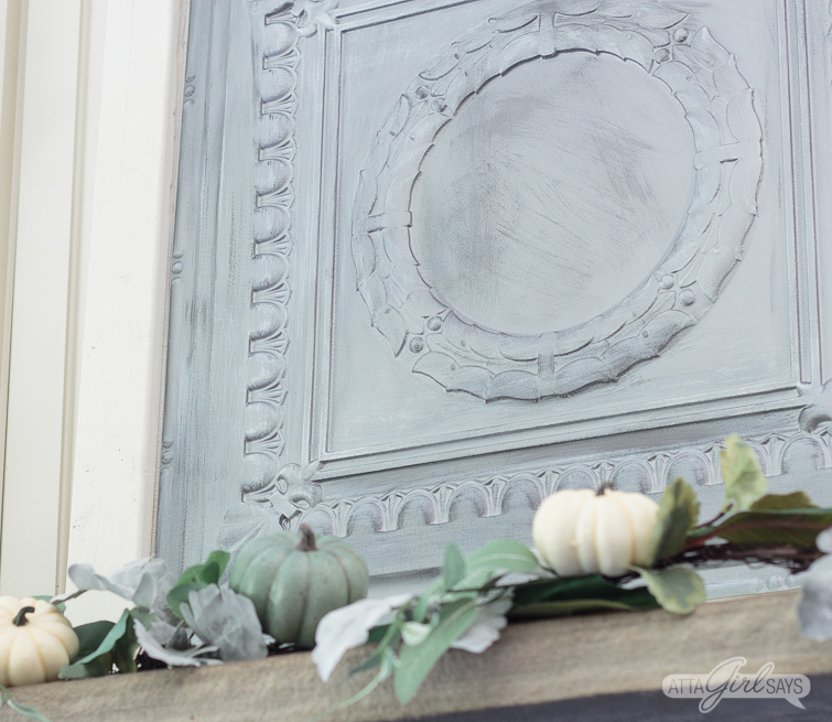 closeup of a silver tin ceiling panel on a fireplace mantel, decorated with a silvery green fall garland
