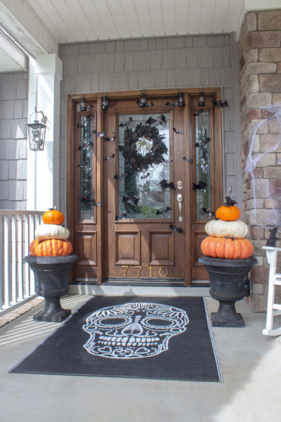 black skeleton rug and two Cinderella pumpkin topiaries in black urns on a Halloween front porch