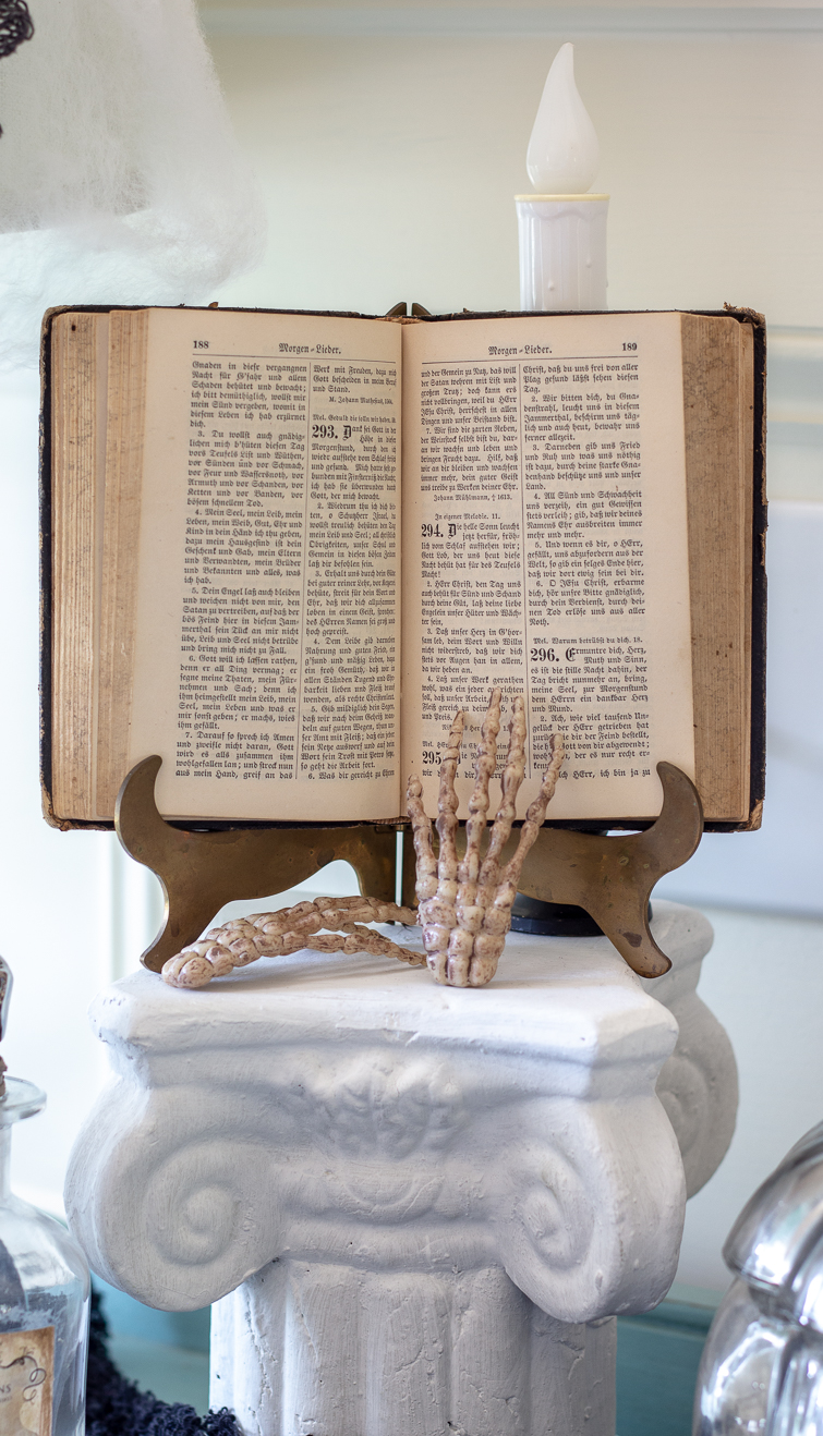 German book on a brass stand atop a plaster column with skeleton hand