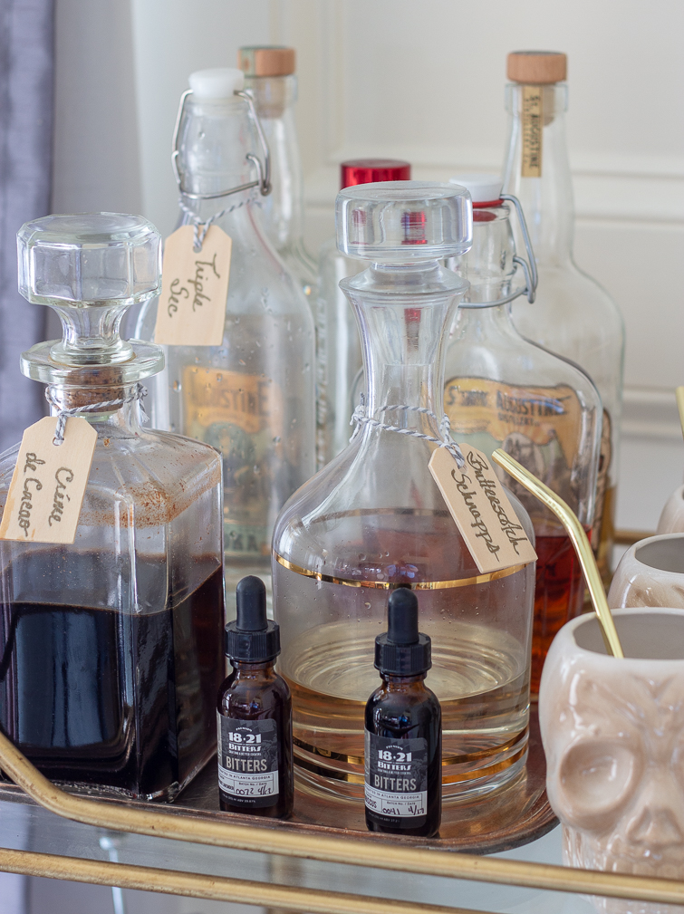 bitters and liquor in glass decanters on a gold bamboo bar cart