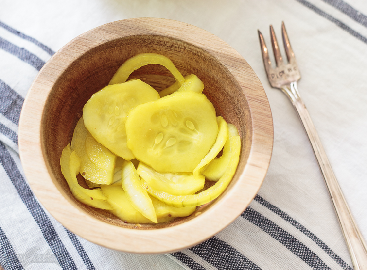 overhead view of overnight refrigerator pickles in a small wooden bowl with a tiny silver pickle fork