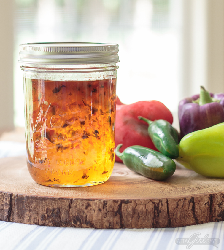 jar of homemade pepper jelly on a wooden slice with a cluster of colorful peppers