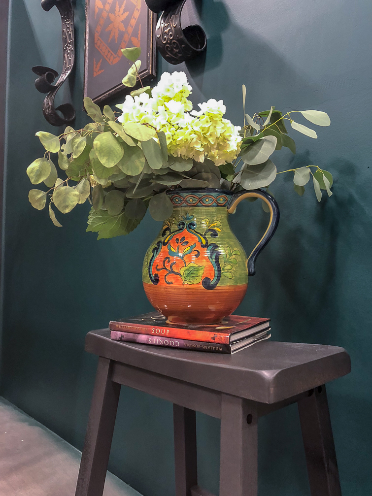 eucalyptus and white hydrangeas in an Italian pitch on top of a dark gray stool
