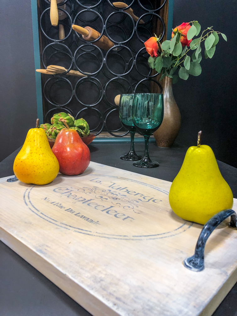 whitewashed cutting board with pears sitting on it in front of a wine rack