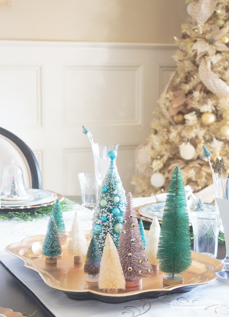 aqua and white bottlebrush Christmas trees on a gold tray on a dining room table with a gold Christmas tree in the background