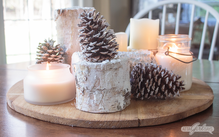 winter centerpiece created using snowy birch logs, pinecones, candles on a bread board