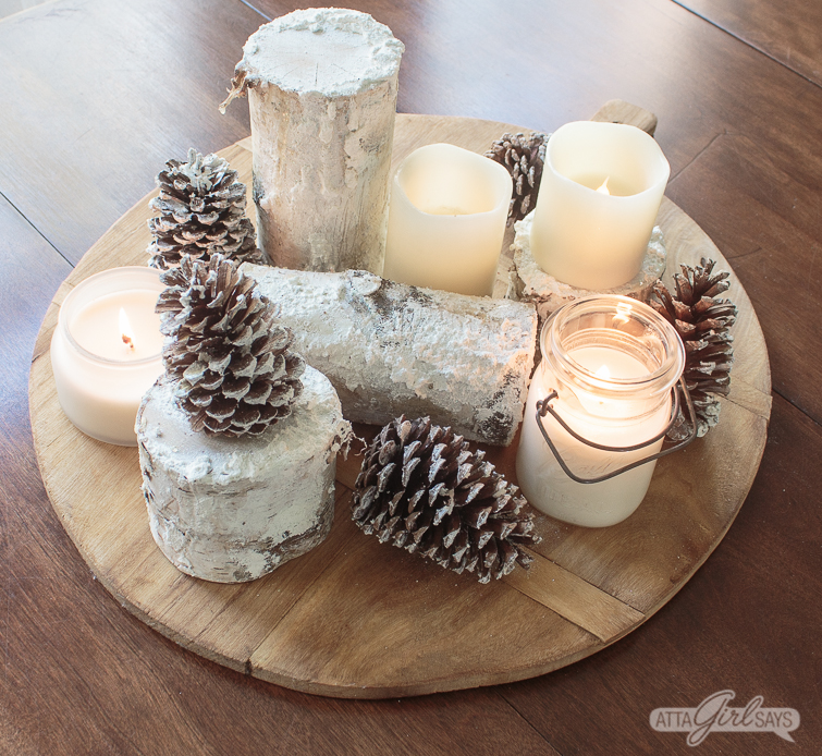 winter centerpiece created using snowy birch logs, pinecones, candles on a bread board