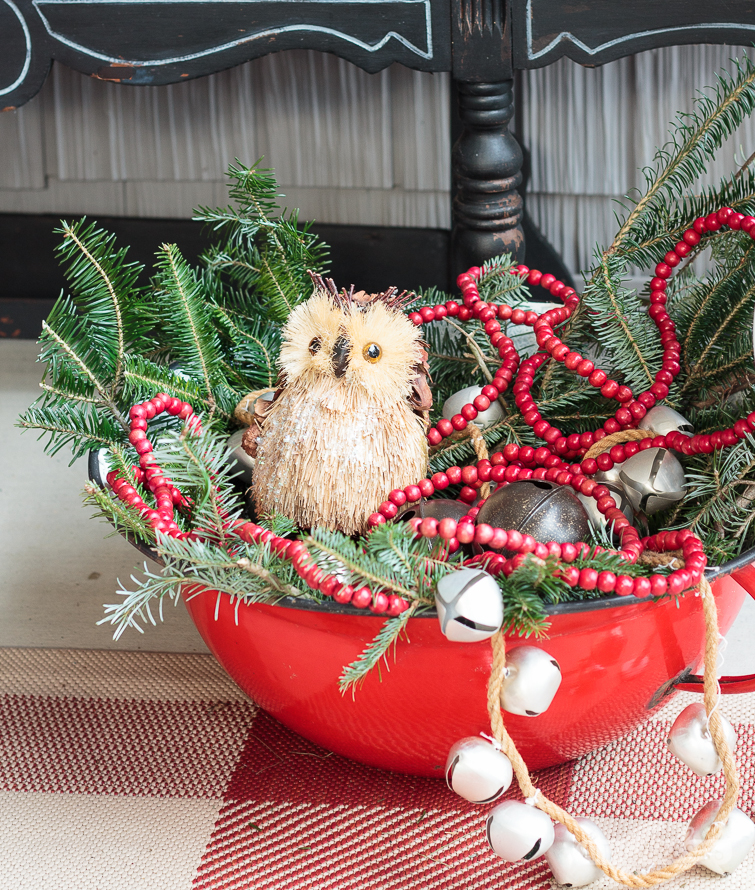 vintage red enamel bowl filled with Christmas greens, bells, red wooden beads and a woodland owl ornament