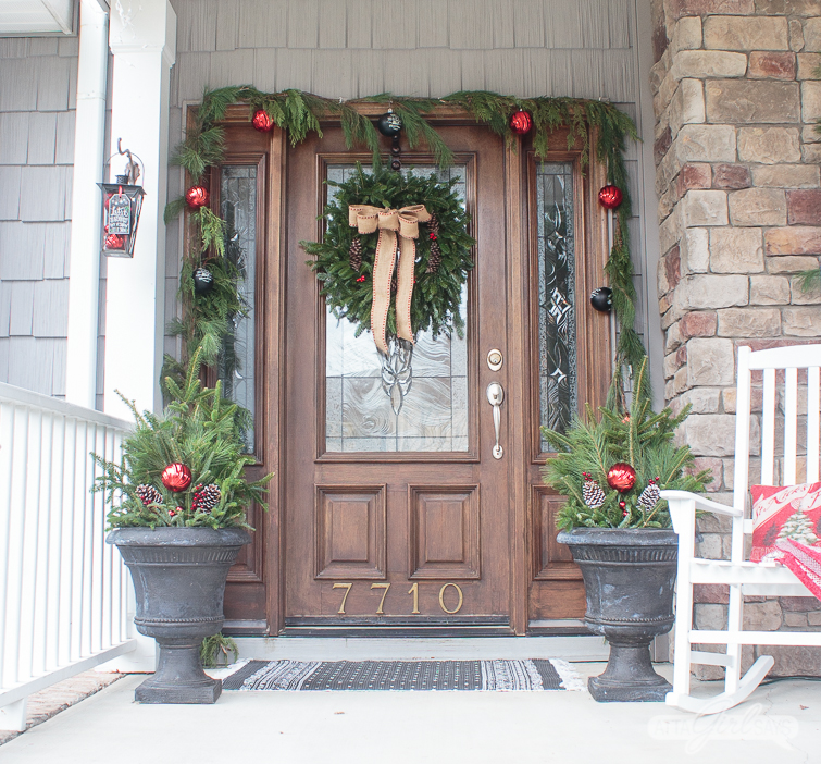 front door decorated with an evergreen wreath, garlands and black urns for Christmas