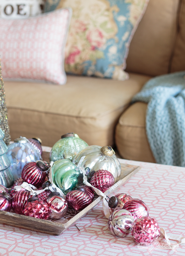 pink mercury glass garland and oversized Christmas ornaments on a tray in front of a sofa