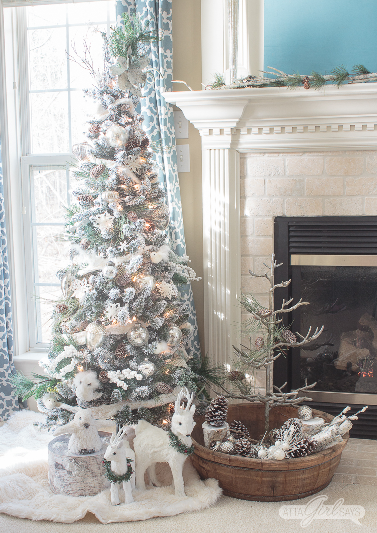 white flocked Christmas tree beside a fireplace in a bedroom with blue curtains