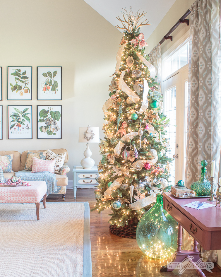 Christmas tree decorated with gold ribbon and pink and green ornaments in a formal living room
