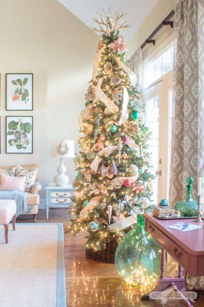 Christmas tree decorated with gold ribbon and pink and green ornaments in a formal living room