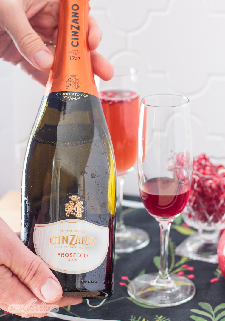 man holding a bottle of prosecco before making a pomegranate mimosa
