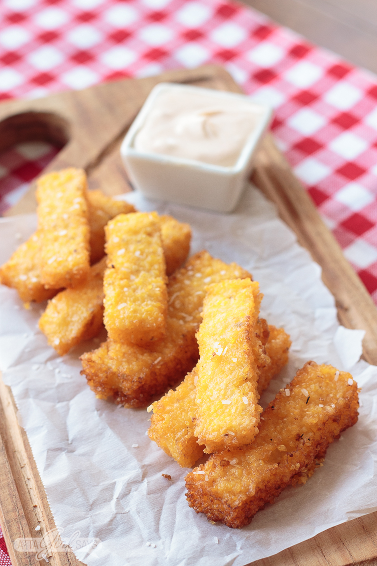 overhead shot of a grit fries stacked on a wooden board with a spicy dipping sauce