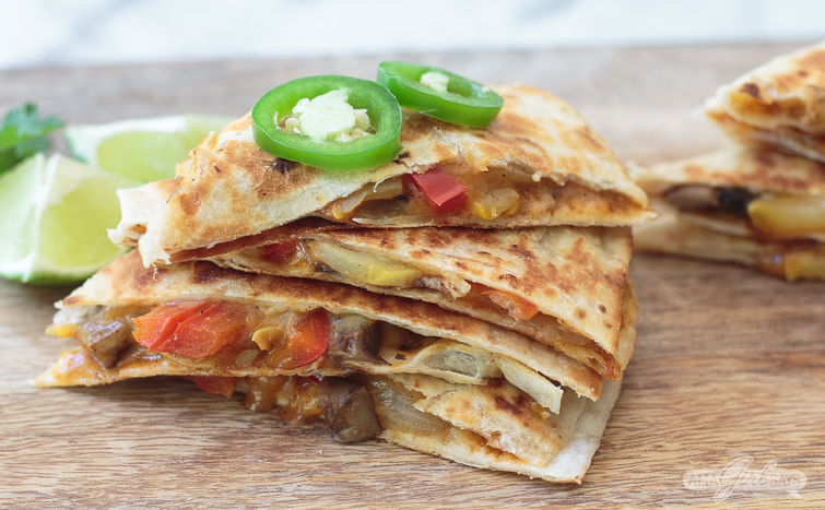 veggie quesadilla cut in wedges and topped with sliced jalapenos on a wooden board