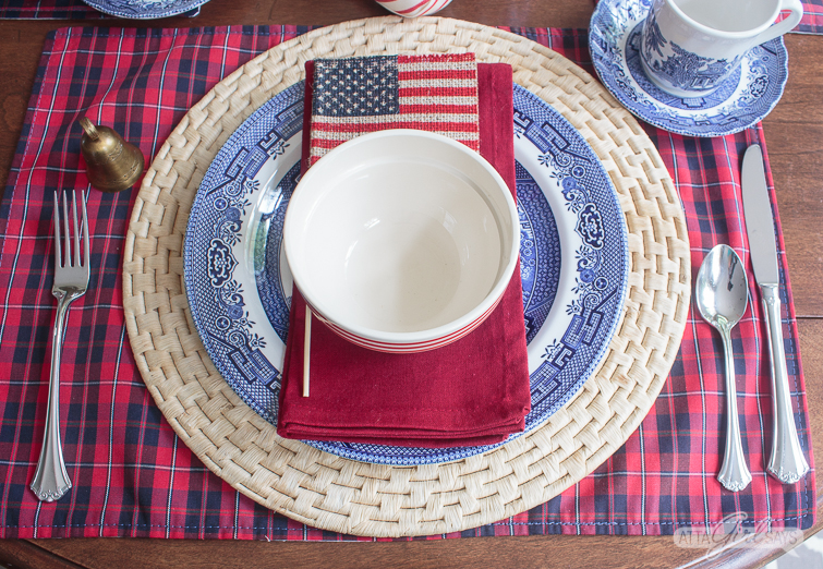 4th of July table decoration with a Blue Willow Plate, red napkin, bowl and flag on a straw charger