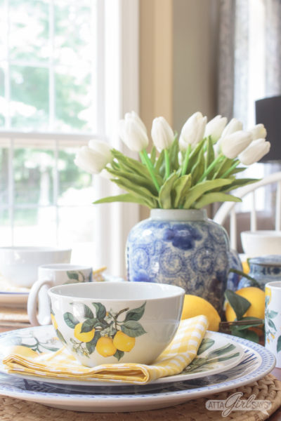 yellow lemon bowl on a dining table with a blue and white vase of tulips in the background