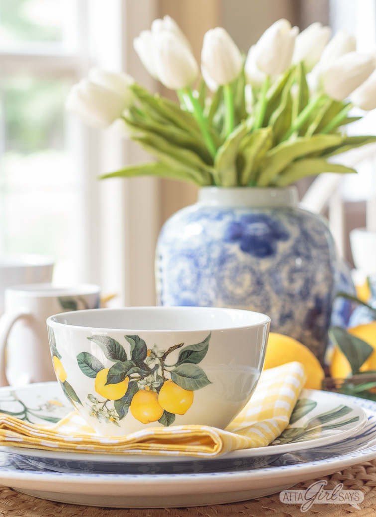yellow lemon bowl on a dining table with a blue and white vase of tulips in the background