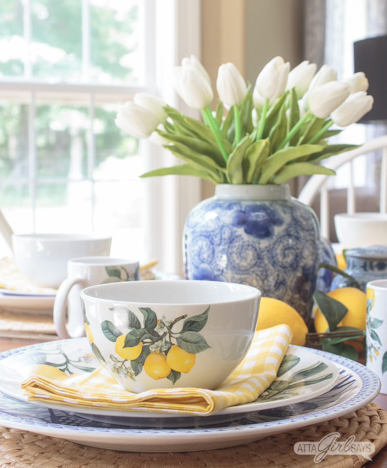 yellow lemon bowl on a dining table with a blue and white vase of tulips in the background