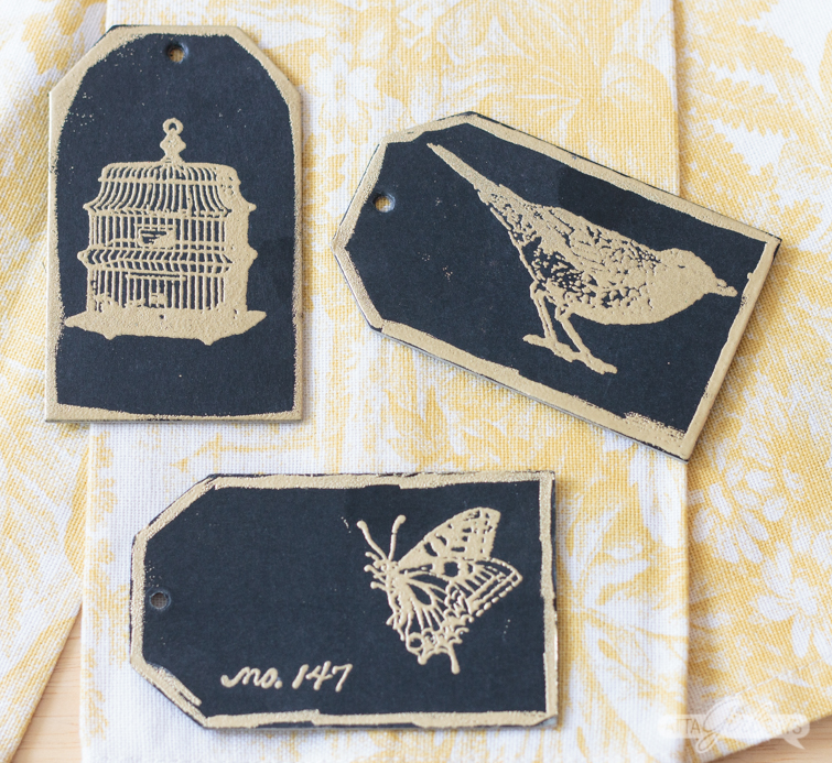 black cardstock tags with gold embossed bird, butterfly and birdcage images on them