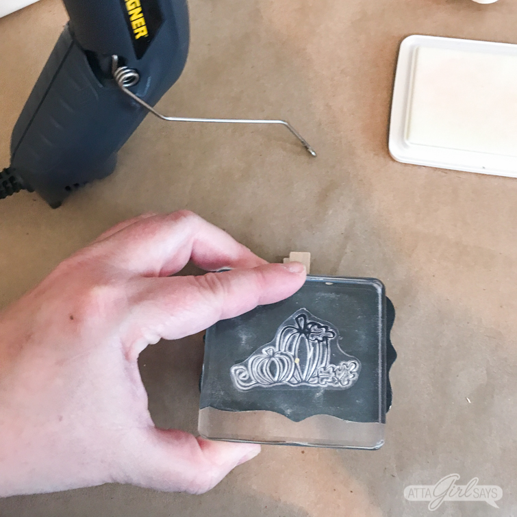 stamping a pumpkin design with embossing ink on a chalkboard clip