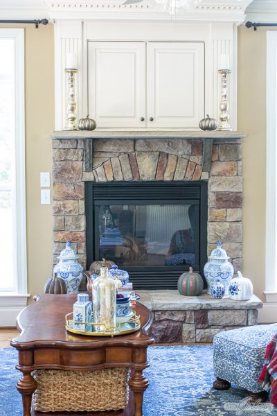 store fireplace with a TV cabinet over it decorated for fall with blue and white chinoiserie and copper pumpkins