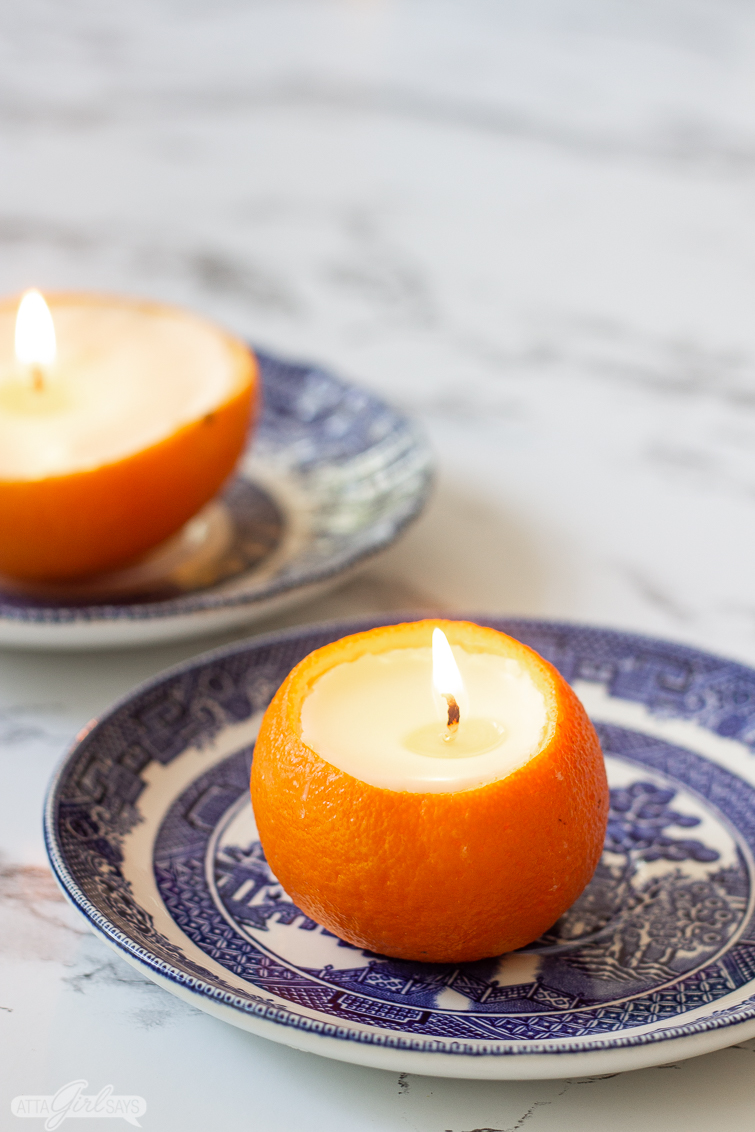 mandarin orange candle on a blue china plate with a navel orange scented candle in the background on a marble countertop