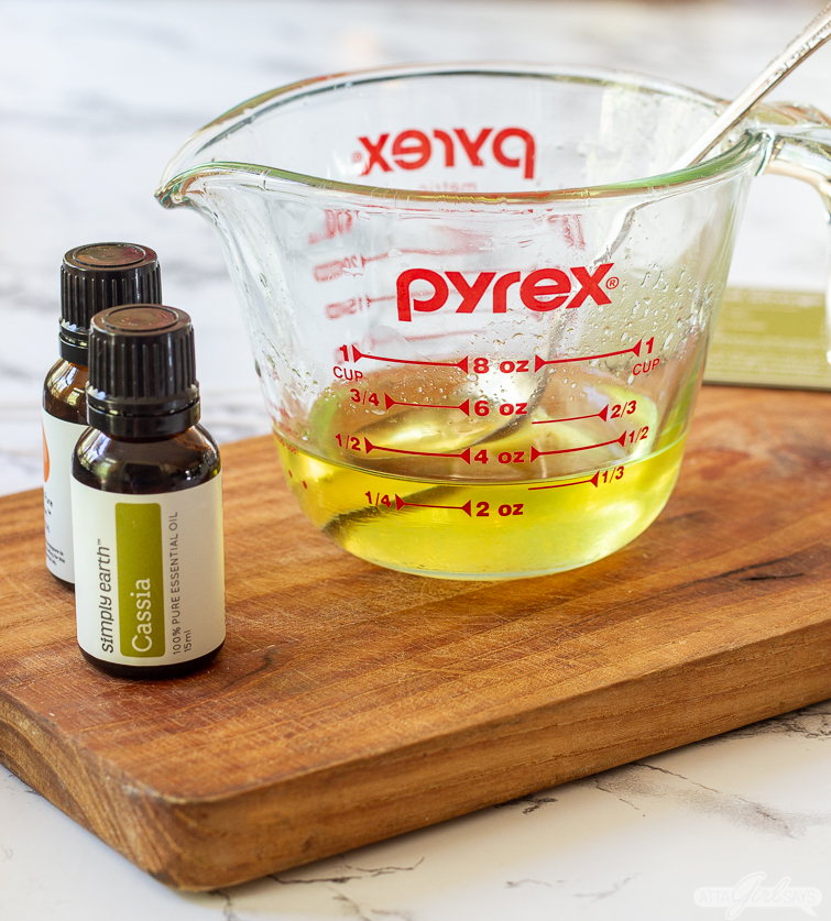 measuring cup of melted wax beside two bottles of essential oils