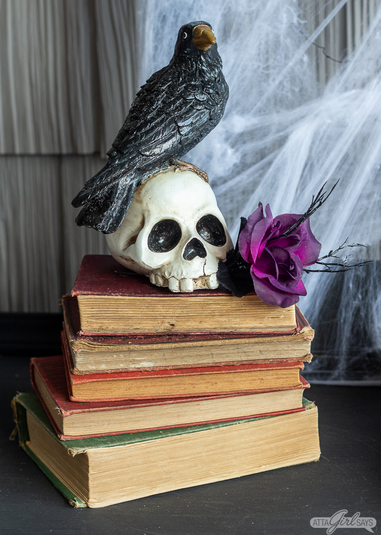 raven sitting on a skull on a stack of old books as part of Halloween front porch decorations