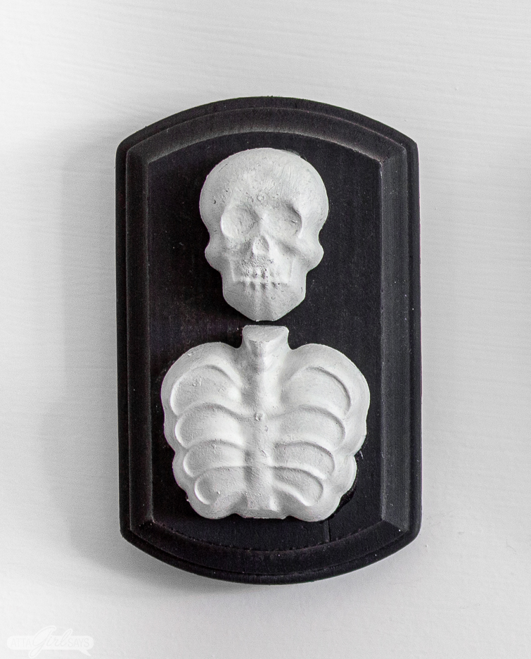 resin skeleton on a black wooden plaque made with dollar store Halloween decorations