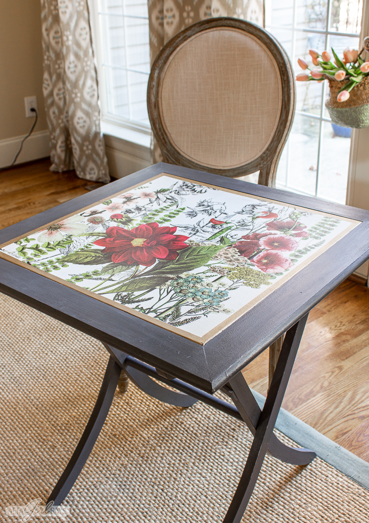 square folding table with a floral inset top beside a Louis chair