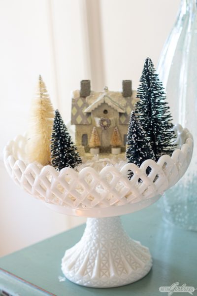 bottlebrush Christmas trees and a paper house displayed in a milk glass compote for Christmas