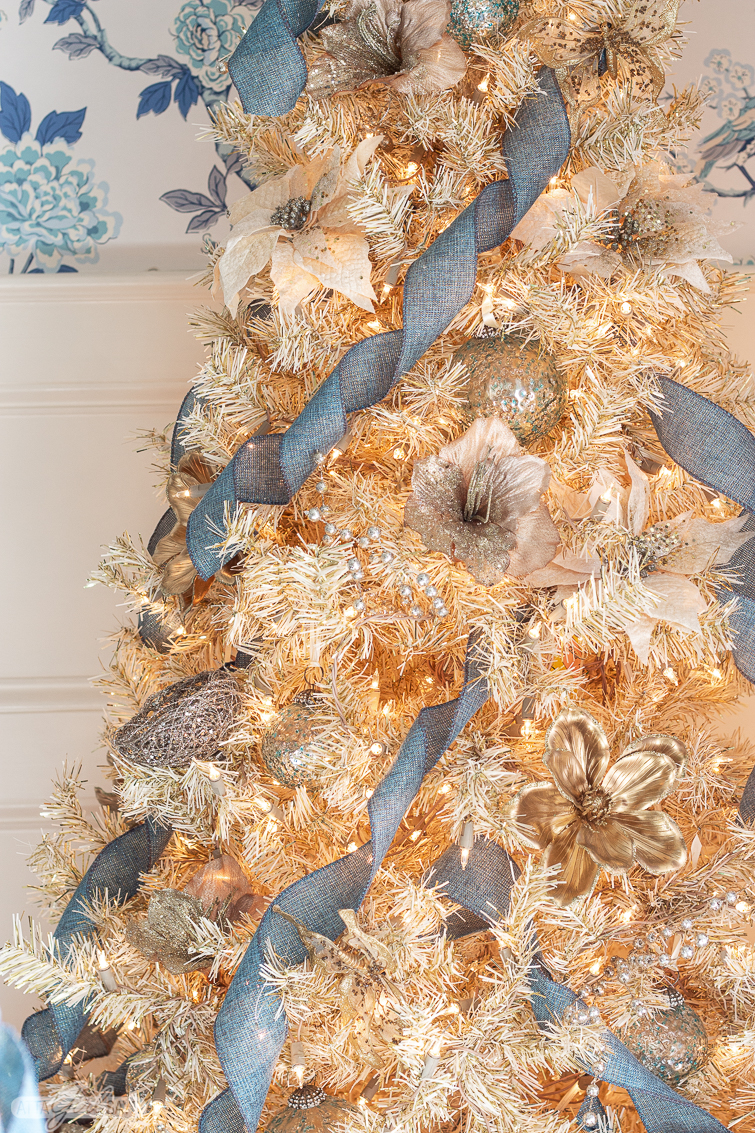 gold Christmas tree decorated with blue ribbon, gold flowers and birds in a formal dining room with toile wallpaper